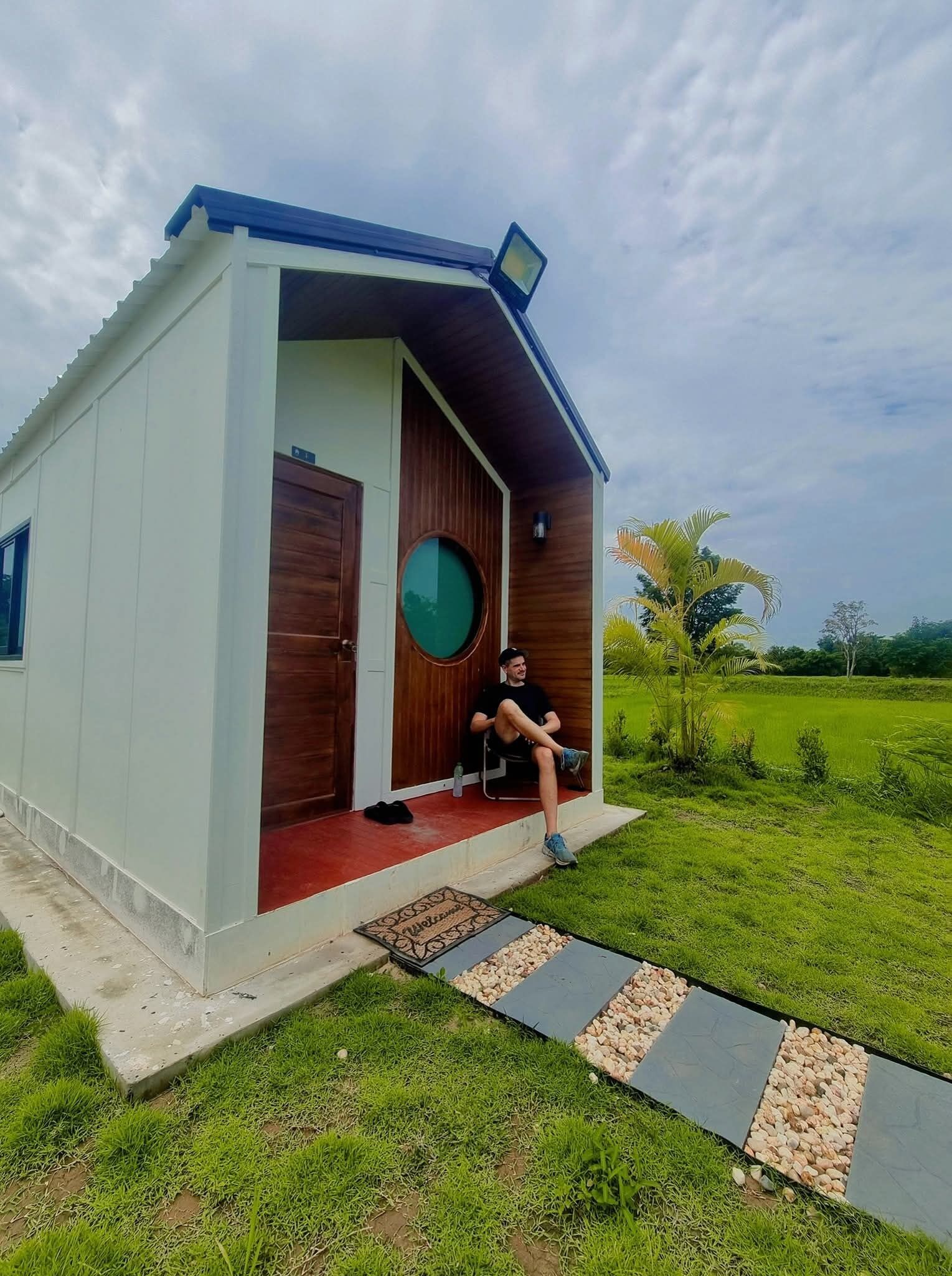 A modern house with a large wooden door, a circular window, and a person sitting on a chair outside.