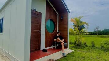 A modern house with a large wooden door, a circular window, and a person sitting on a chair outside.