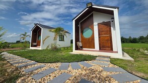 Two modern, single-story buildings with large windows and wooden doors, surrounded by a well-maintained garden and a stone pathway. - The Garden Resort  (Nong Rua)