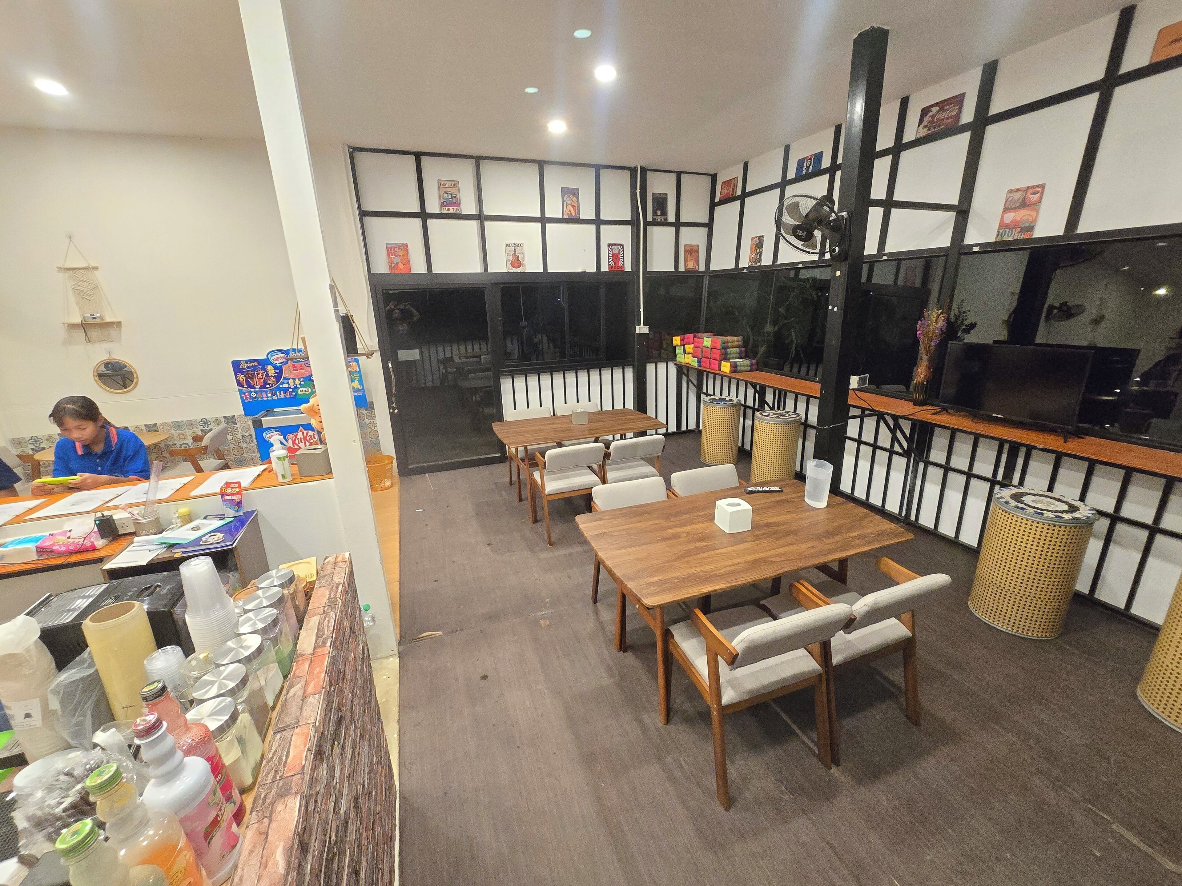 A restaurant interior with wooden tables and chairs, a counter with various items, and a wall decorated with framed pictures.