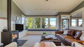 Ein modernes Wohnzimmer mit Kamin, Ledersofa und großem Fenster mit Blick auf Grünflächen.