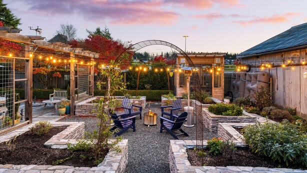 Eine Gartenpatio mit Adirondack-Stühlen, einem Feuerkorb und Lichterketten.