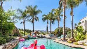 Una piscina con un flotador de flamenco rosa, rodeada de palmeras y sillas de descanso.