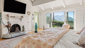 Un dormitorio con una cama grande, chimenea, televisor y balcón con vistas a la montaña.
