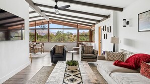 A spacious living area with a large window, a ceiling fan, and a view of the outdoors. - Luxe Red Rock Views, Heated Pool & Spa, Hot tub (Sedona)