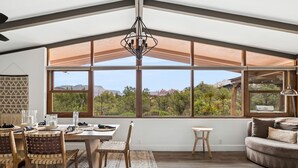 A spacious room with a large window offering a view of the outdoors, a dining area with a table and chairs, and a cozy seating area with a sofa. - Luxe Red Rock Views, Heated Pool & Spa, Hot tub (Sedona)