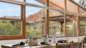 A dining area with a table, chairs, and large windows offering a view of red rock formations. - Luxe Red Rock Views, Heated Pool & Spa, Hot tub (Sedona)