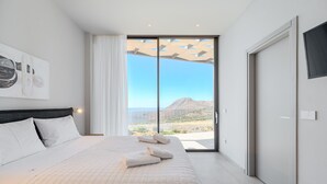 Ein Schlafzimmer mit einem großen Bett, Blick auf die Berge und einer Schiebetür zu einem Außenbereich.