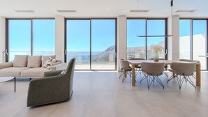 Ein großzügiger Wohnbereich mit einem großen Fenster und Aussicht auf eine reizvolle Landschaft, einem bequemen Sofa und einem Esstisch mit Stühlen.