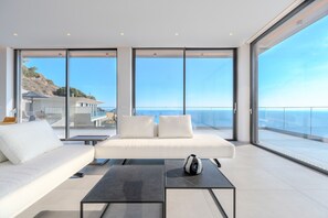 Een moderne woonkamer met een witte bank, twee zwarte salontafels en uitzicht op de oceaan.