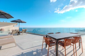 Eine Dachterrasse mit Glasbrüstung, einem Tisch und Stühlen sowie zwei Sonnenschirmen.