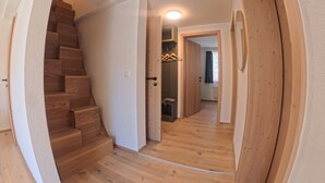 Un couloir doté d’un plancher en bois, d’un escalier et d’une porte donnant sur une autre pièce.