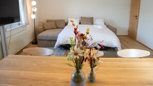 Une chambre à coucher moderne avec un lit, un canapé, une télévision et une table en bois ornée de vases de fleurs.