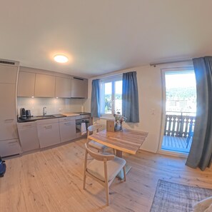 A modern kitchen with a dining area, wooden flooring, and a view of a balcony.