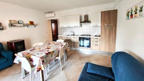 Una cocina compacta con comedor, armarios blancos y un sofá azul.