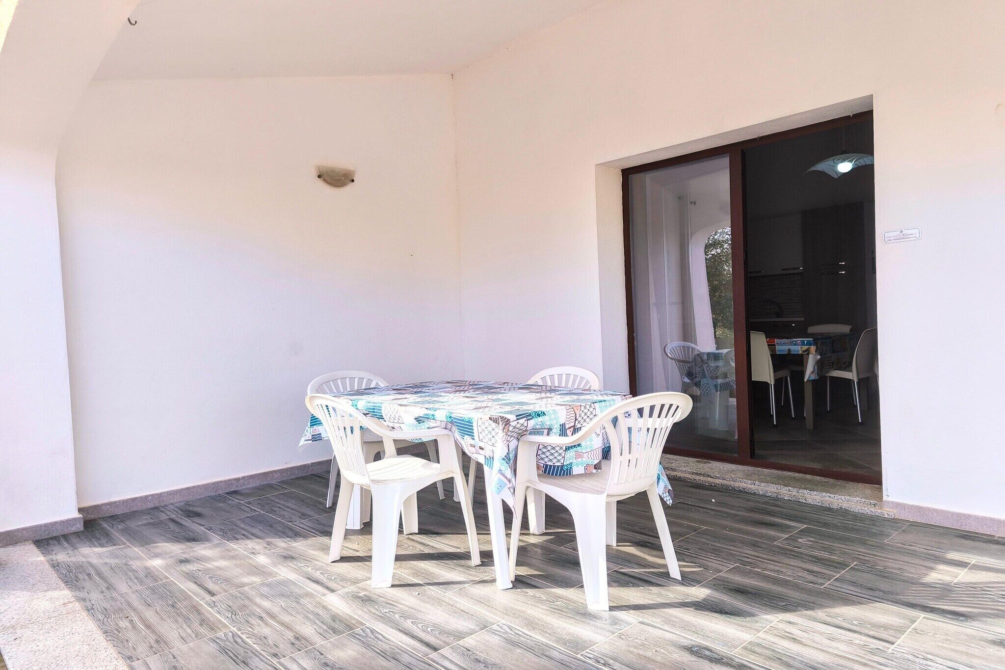 Eine überdachte Terrasse mit Tisch und Stühlen, eine Glastür zum Innenbereich und ein gefliester Boden.