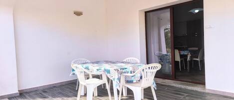 Eine überdachte Terrasse mit Tisch und Stühlen, eine Glastür zum Innenbereich und ein gefliester Boden.