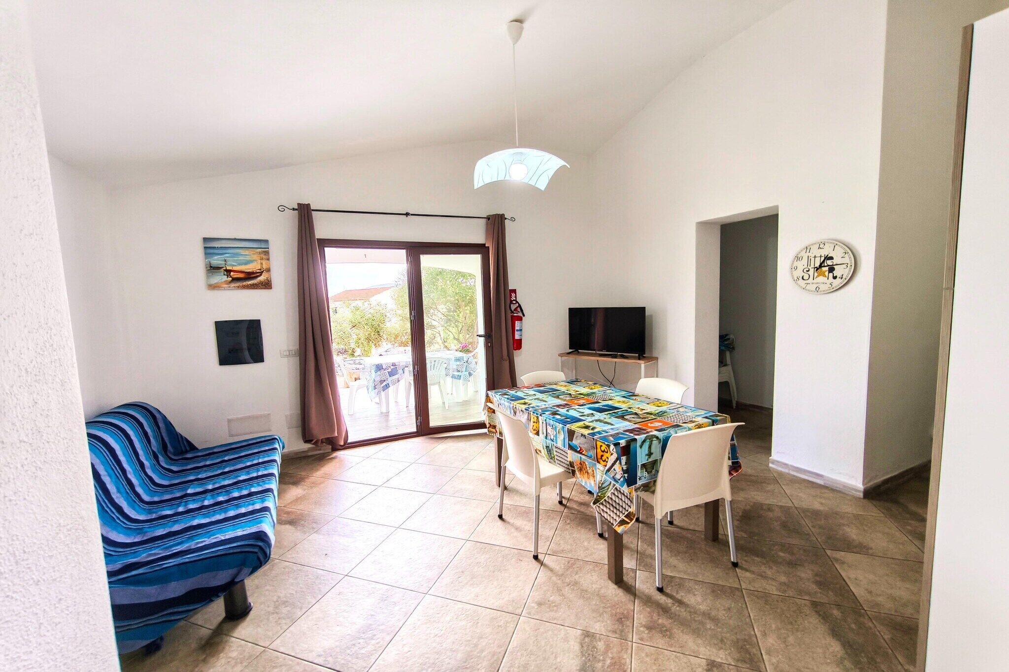 Une pièce comprenant une table à manger, des chaises, un canapé, un téléviseur et une porte donnant sur un espace extérieur.