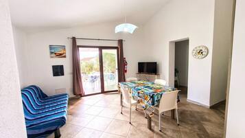 Une pièce comprenant une table à manger, des chaises, un canapé, un téléviseur et une porte donnant sur un espace extérieur.
