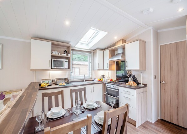 A modern kitchen with a skylight, built-in microwave, and a dining area with wooden chairs and a table set for two. - 2 bedroom accommodation in Bala, (Bala,)