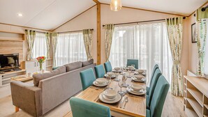 Un coin repas avec une table en bois dressée pour quatre personnes, un canapé et un téléviseur en arrière-plan.