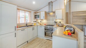 Une cuisine moderne avec des meubles blancs, un plan de travail en bois, une cuisinière, un four et une fenêtre avec des stores.
