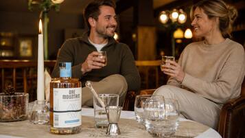 Two people seated at a table with a bottle of liquor, glasses, and a candle.