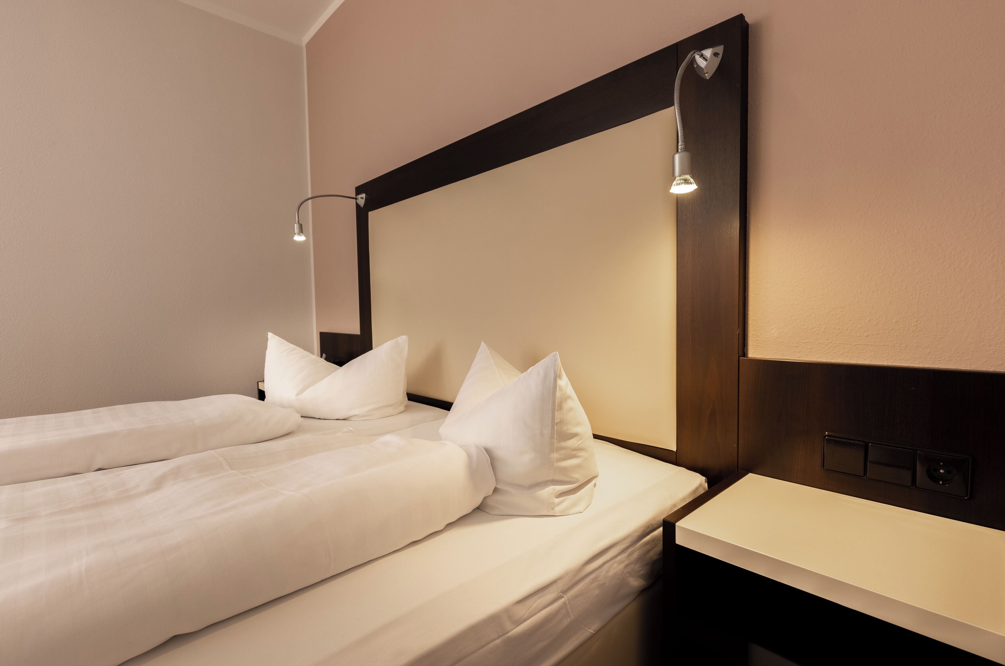 A hotel room with two single beds, a bedside table, a nightstand, and a large mirror above the bed.