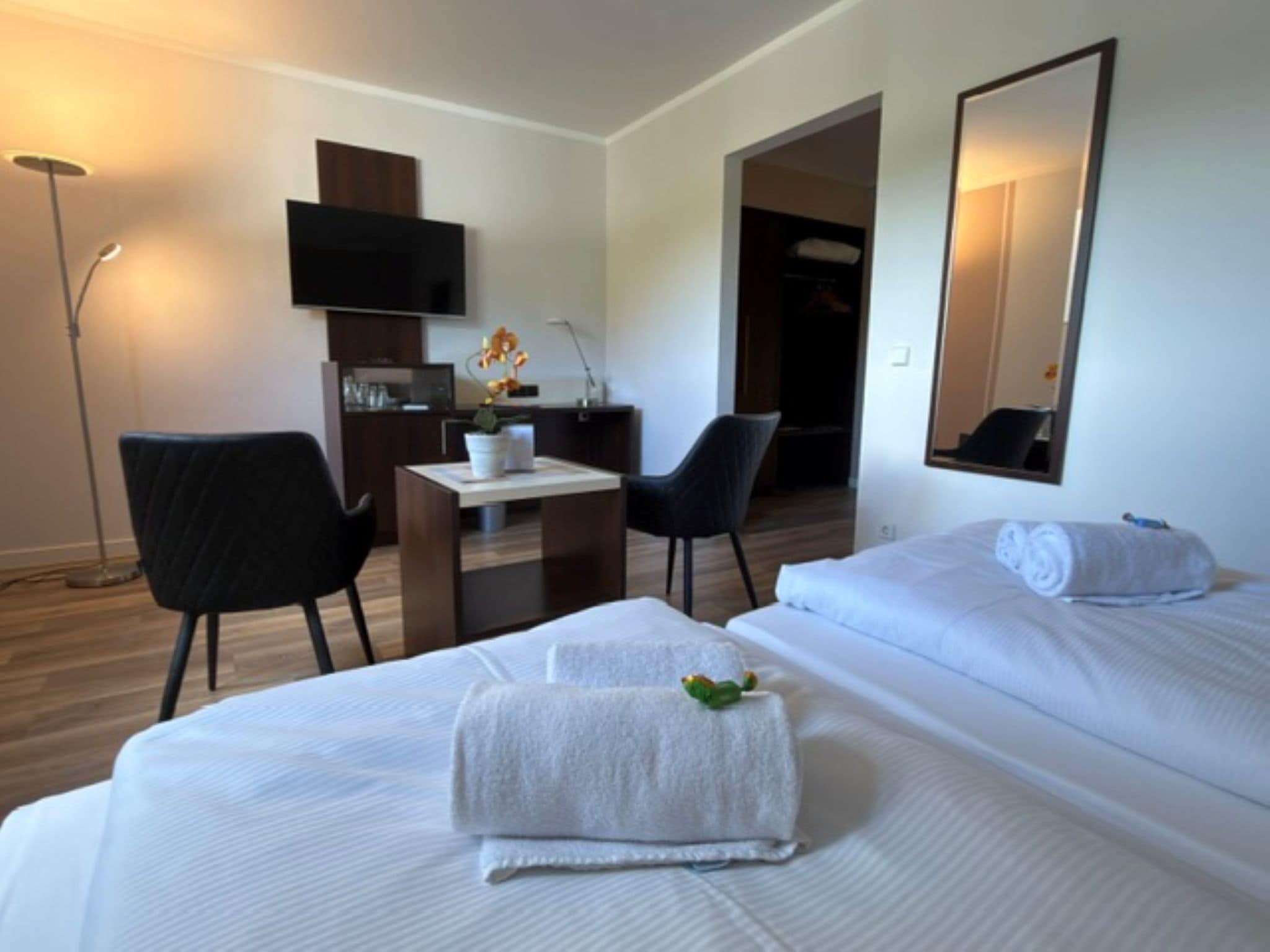 Ein Hotelzimmer mit Bett, Schreibtisch, zwei Stühlen, Fernseher und Spiegel.