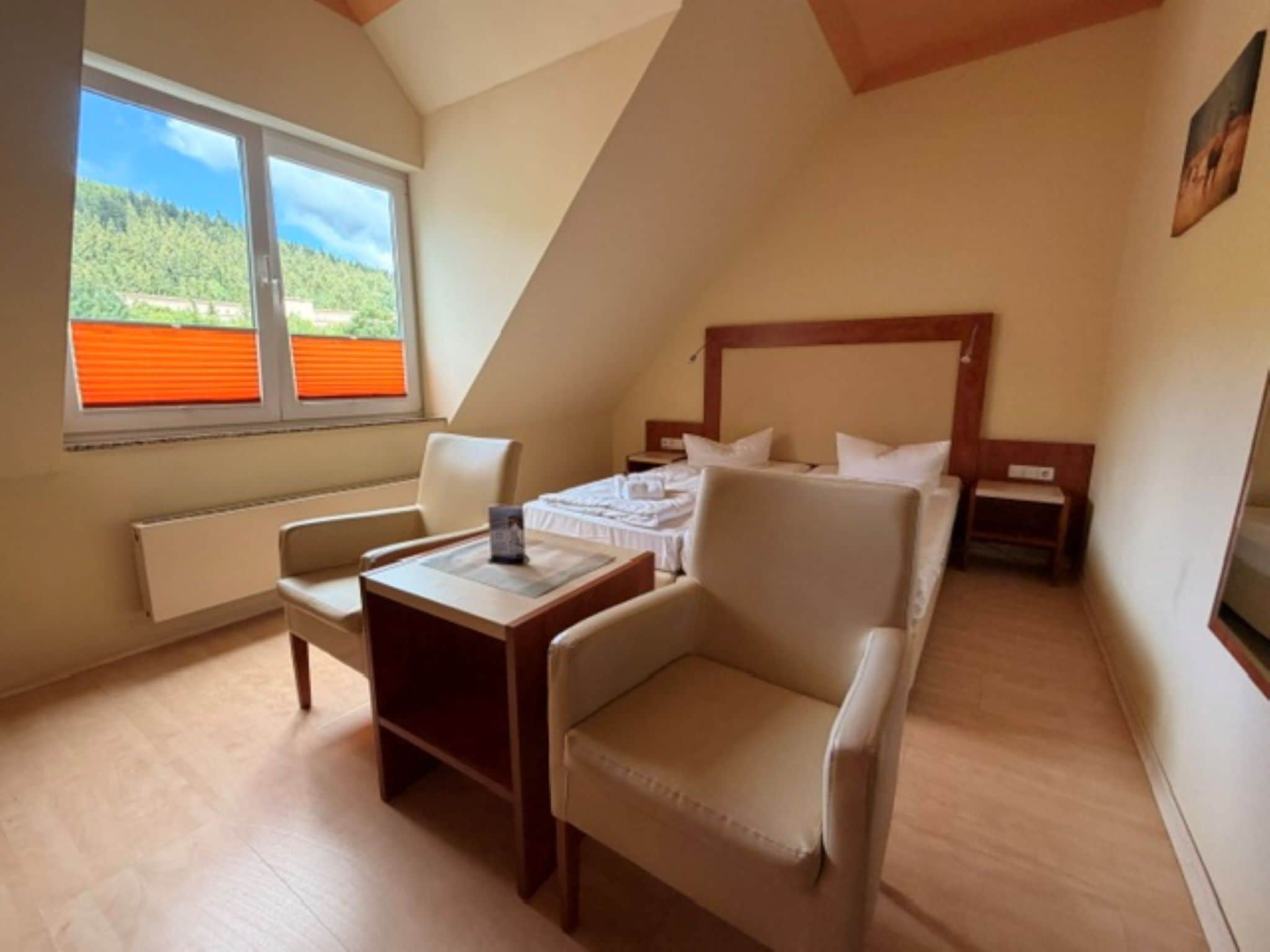 A small, cozy room with a bed, a chair, a table, and a window with a view of greenery.
