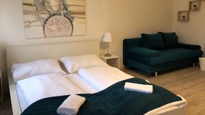 A hotel room with a bed, a green sofa, a small table with a lamp, and a wall-mounted artwork. - Stylish Apt Near Wiener Stadthalle (Vienna)