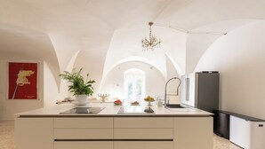 Een moderne keuken met een centraal eiland, een kroonluchter en een koelkast.