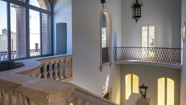 Een statig interieur met een marmeren trap, boogvensters en versierde balustrades.