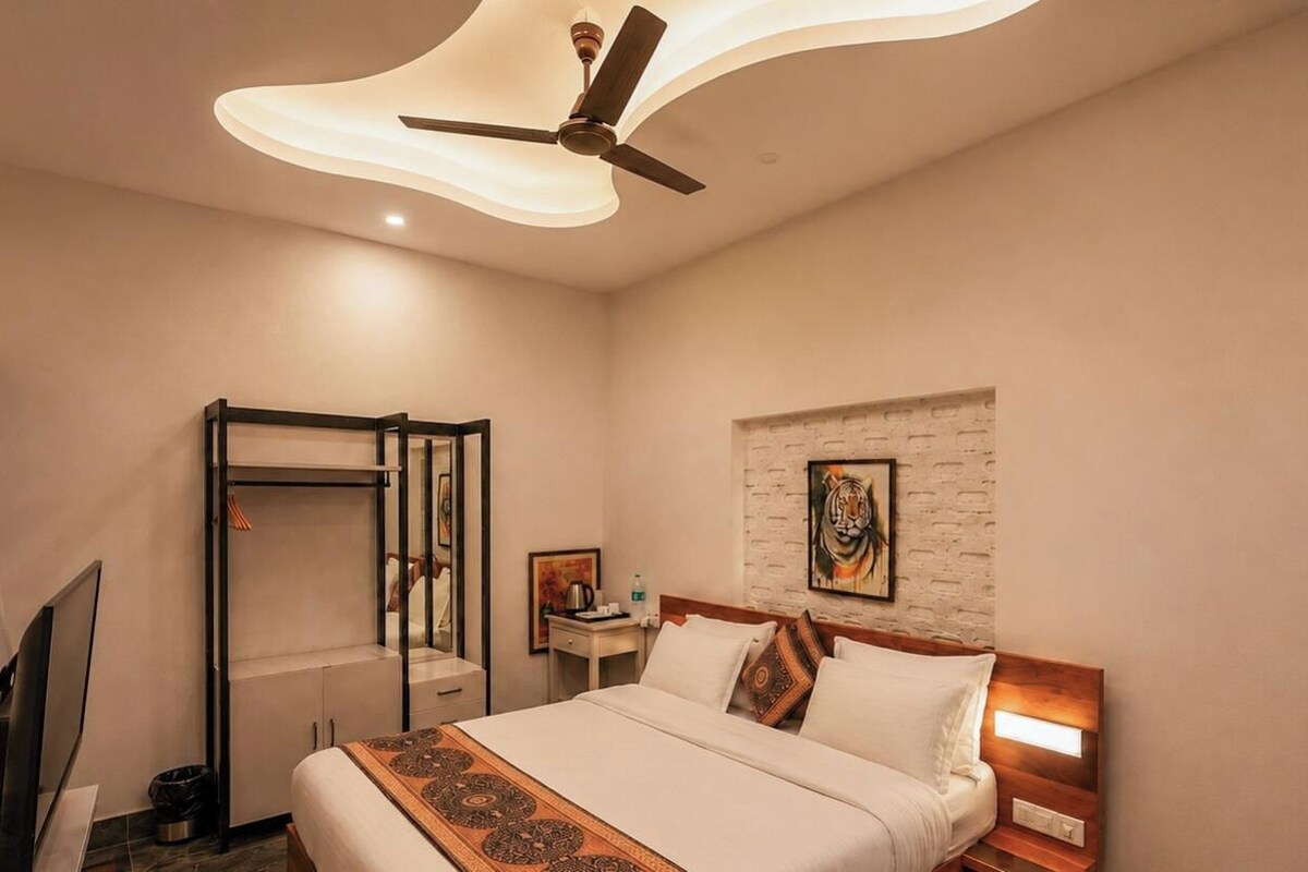 A hotel room with a bed, a desk, a chair, a ceiling fan, and a wall-mounted artwork.