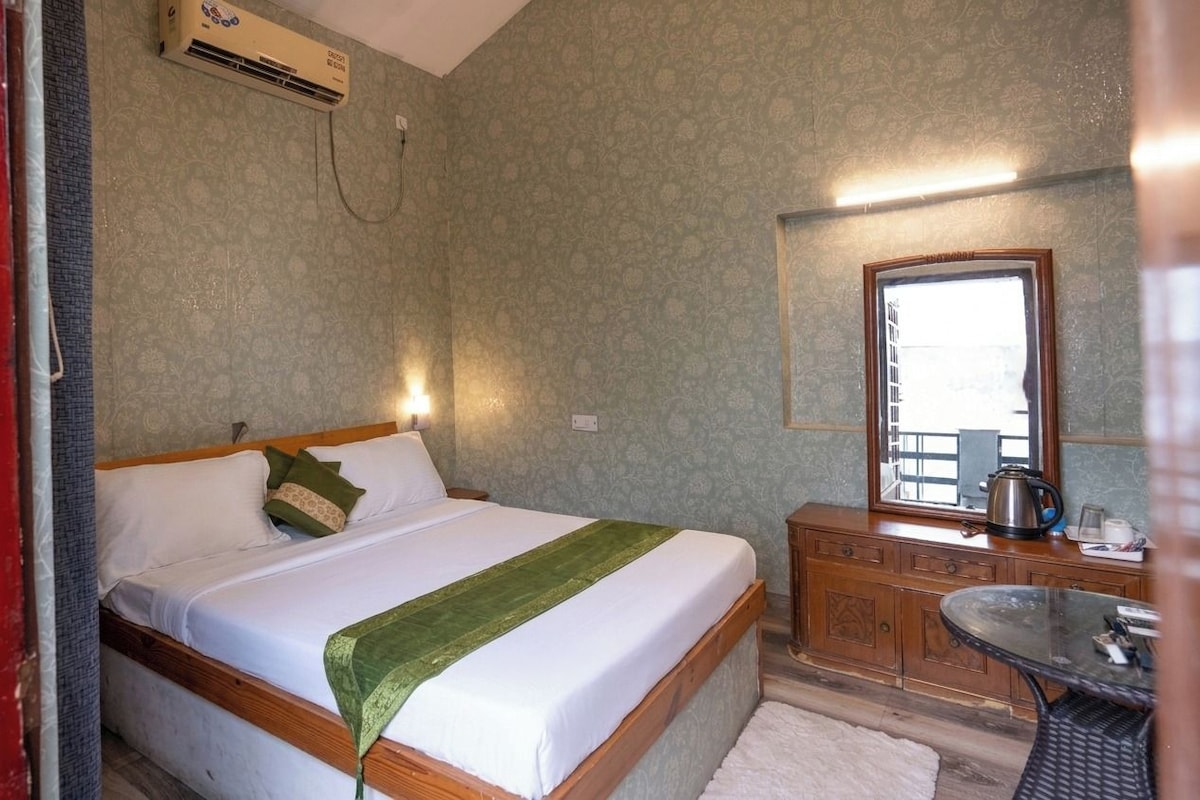 A bedroom with a bed, a bedside table, a mirror, and an air conditioning unit.