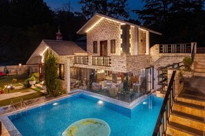 Une maison en pierre à deux étages, dotée d’une piscine, d’un espace salon extérieur et d’un escalier menant à l’étage supérieur.