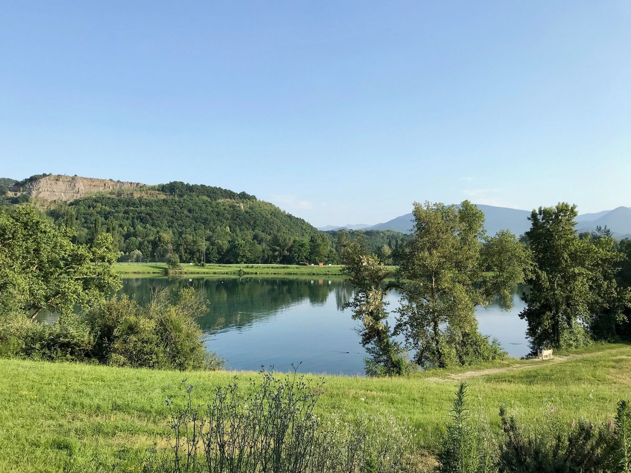 Un paysage paisible avec un lac, une vég étation luxuriante et des collines qui se dessinent à l’horizon.