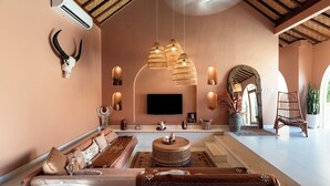 Un salón amplio con techo alto, un televisor de pantalla plana grande y una zona de estar cómoda con sofá y sillón.