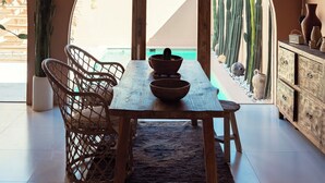 Un comedor con una mesa de madera, sillas de mimbre y una lámpara colgante.