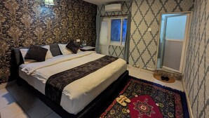 A neatly arranged bedroom with a bed, a nightstand, a window, and a patterned rug. - Luna Hotel And Lounge (Kathmandu)