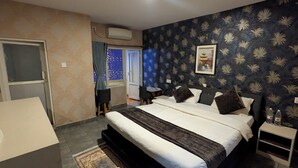 A hotel room with a large bed, a small table, a nightstand, a window with curtains, and a wall with a leaf pattern. - Luna Hotel And Lounge (Kathmandu)