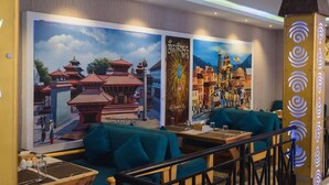 A restaurant with large murals of Asian architecture, teal upholstered seating, and a decorative column with spiral patterns. - Luna Hotel And Lounge (Kathmandu)