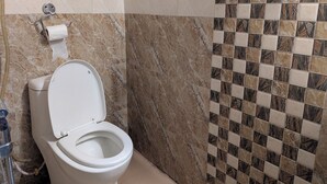 A bathroom with a toilet, a paper towel holder, and a shower area with a tiled wall. - Luna Hotel And Lounge (Kathmandu)