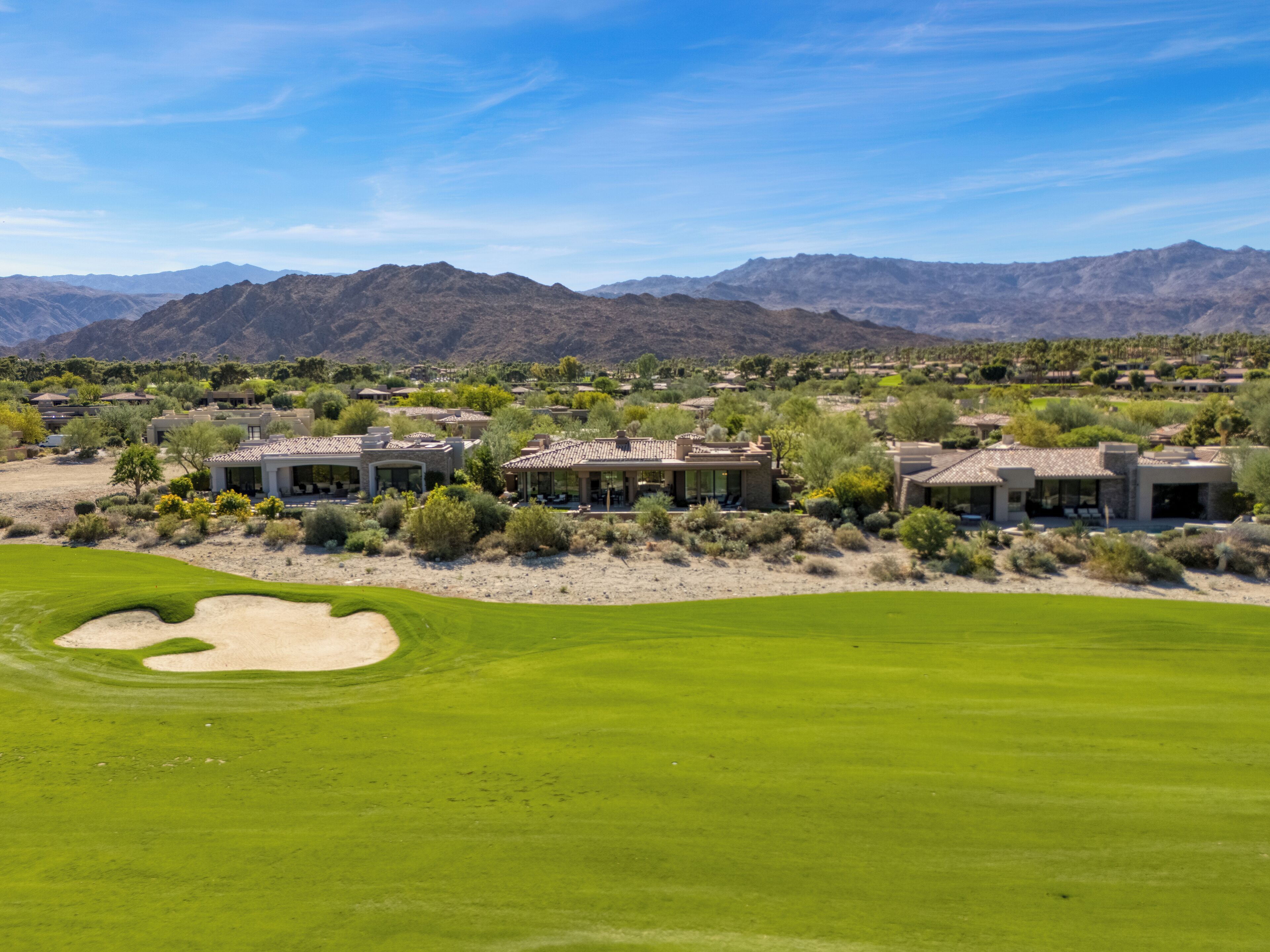A golf course with a desert landscape, multiple buildings, and mountains in the background.