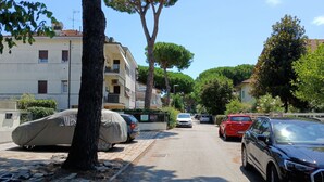 Une rue résidentielle bordée d’arbres, avec des voitures garées le long du trottoir et des immeubles à plusieurs étages.