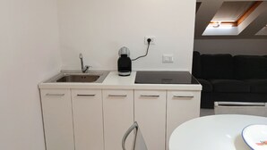 Une petite cuisine moderne équipée d’un évier, d’une machine à café et d’un plan de travail. On y trouve également une chaise et une table avec une assiette.