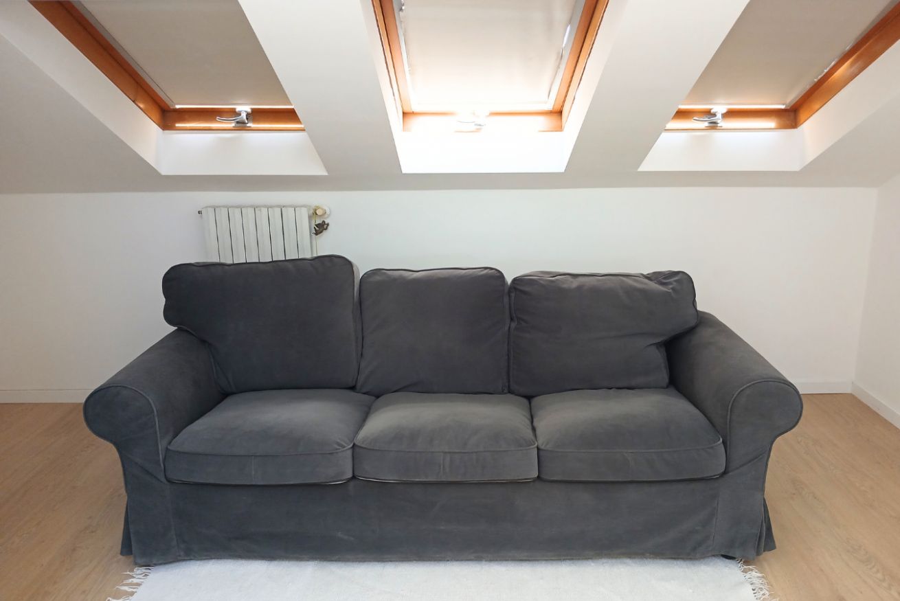Ein graues Sofa in einem Zimmer mit Dachfenster und Heizkörper.