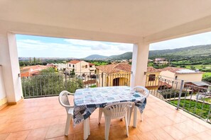 Varanda com mesa e cadeiras, vista para área residencial com casas e vegetação.