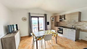 A compact kitchen with a dining table, a TV on a cabinet, and a view through the window. - Apartment with a sea-view terrace (Budoni)