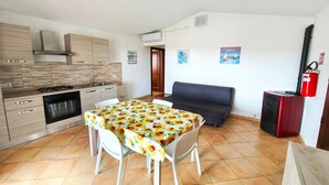 A compact kitchen with a dining area, a sofa, and a small refrigerator. - Apartment with a sea-view terrace (Budoni)